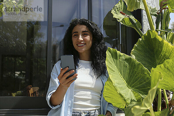 Glückliche Frau benutzt Smartphone inmitten von Pflanzen