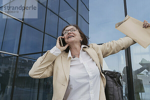 Glückliche Geschäftsfrau  die vor dem Bürogebäude mit ihrem Smartphone spricht