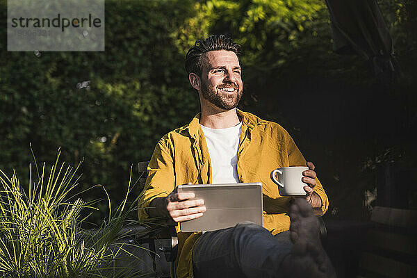 Glücklicher Mann sitzt mit Tablet-PC und Kaffeetasse
