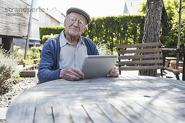 Lächelnder älterer Mann sitzt mit Tablet-PC am Tisch