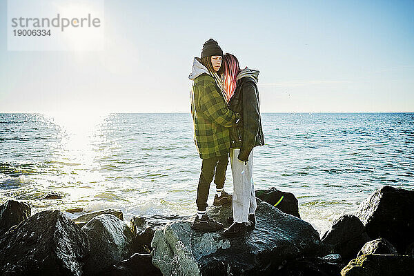 Lesbisches Paar steht zusammen auf Felsen am Meer