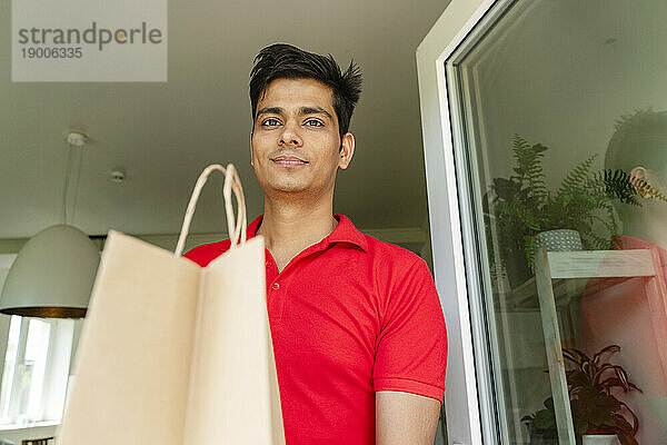 Lächelnder Mann hält Einkaufstüte zu Hause