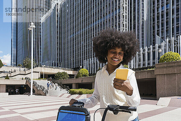 Glückliche Geschäftsfrau mit Elektrofahrrad und Mobiltelefon im Büropark