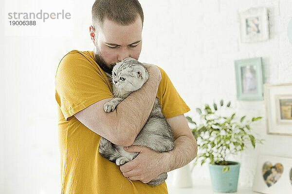 Mann umarmt und küsst Katze zu Hause