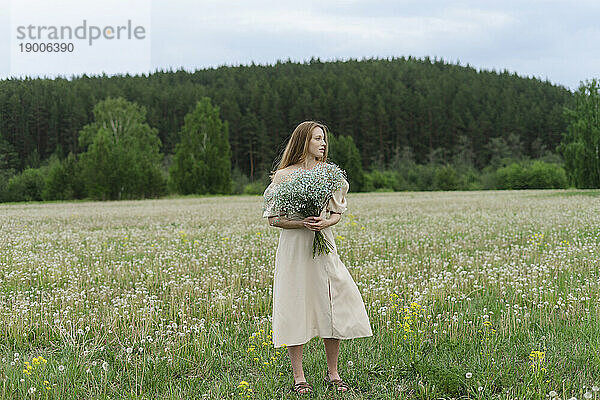 Beautiful young woman holding flower bouquet on field