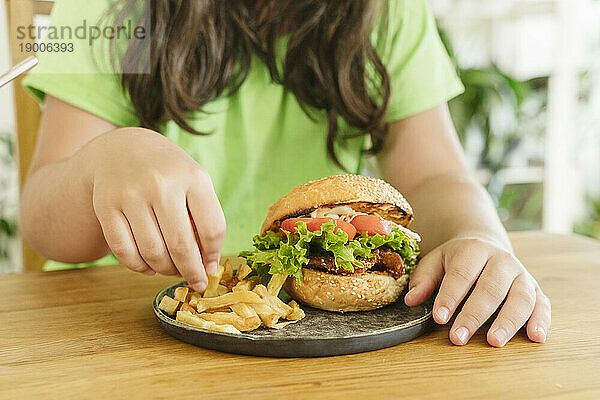 Mädchen isst Pommes und Burger zu Hause auf dem Tisch