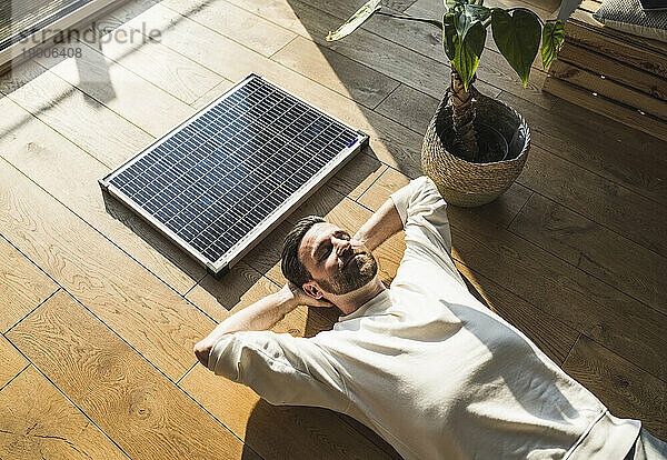Lächelnder Freiberufler entspannt sich zu Hause am Solarpanel