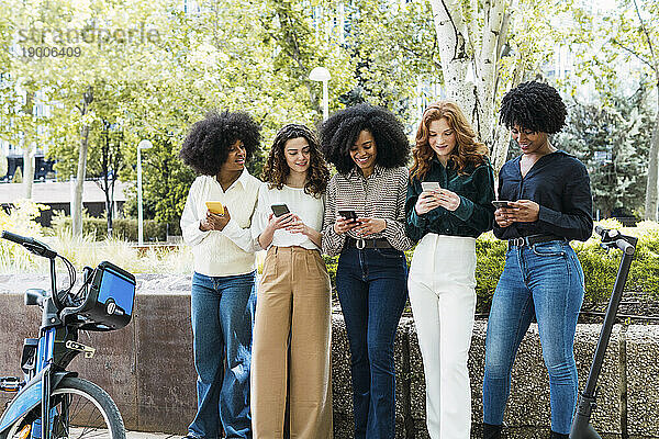 Fröhliche junge Freunde nutzen gemeinsam ihr Smartphone im Park