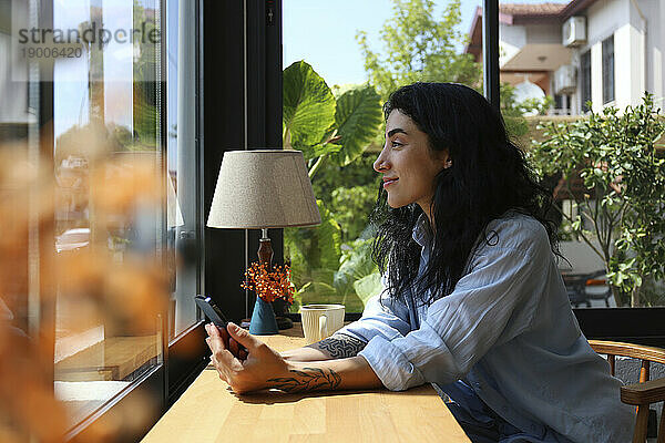 Lächelnde Frau  die im Café aus dem Fenster schaut