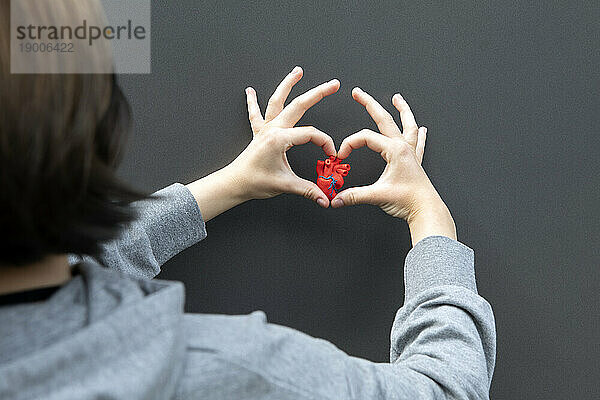 Teenage girl gesturing heart shape on gray background