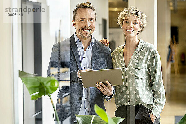 Glücklicher Geschäftsmann und Geschäftsfrau  die mit Tablet-PC im Büro stehen