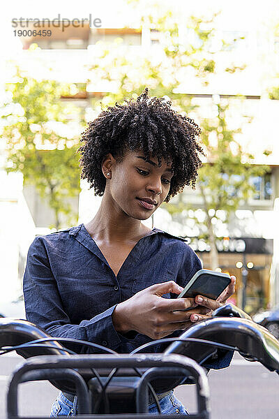 Junge Frau mietet Elektrofahrrad und nutzt Smartphone