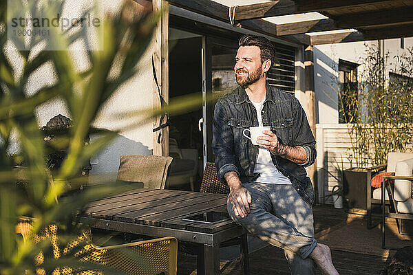 Nachdenklicher Mann sitzt mit Kaffeetasse auf der Terrasse