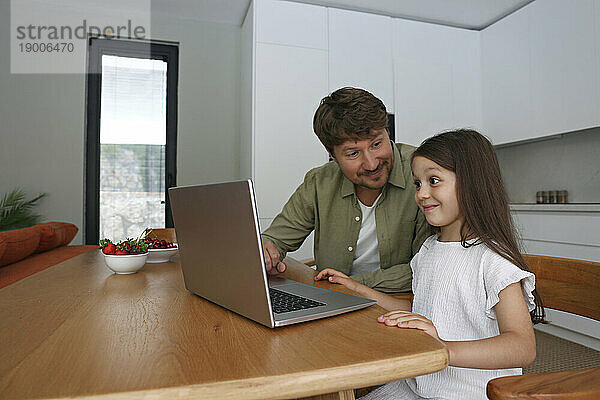 Lächelndes Mädchen  das mit seinem Vater zu Hause lernt  einen Laptop zu benutzen