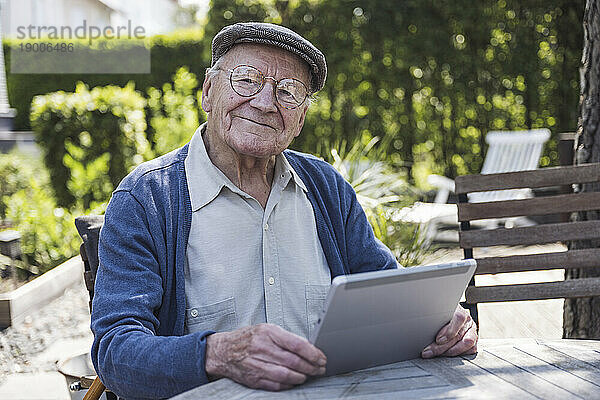 Smiling senior man sitting with tablet PC at table in back yard