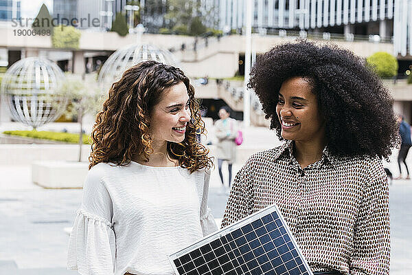 Glückliche Geschäftsfrauen stehen mit Solarpanel im Büropark
