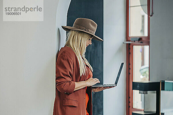 Blonde Frau benutzt Laptop und steht an der Wand