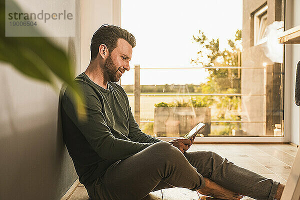 Lächelnder Mann benutzt Tablet-PC auf dem Boden