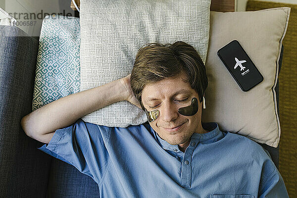 Smiling man with eye patch sleeping next to smart phone on bed at home