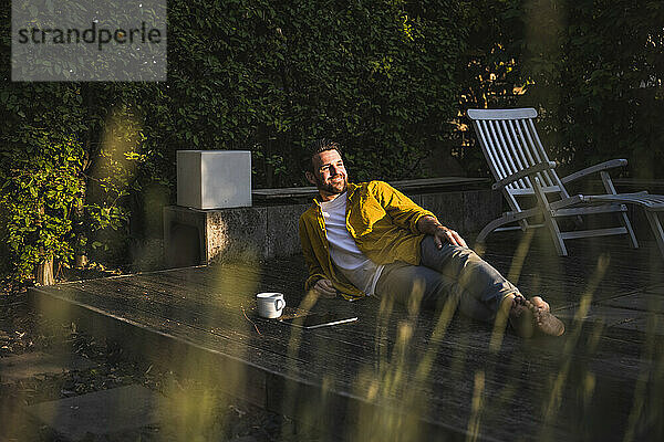 Glücklicher Mann mit Kaffeetasse und Tablet-PC entspannt auf der Veranda