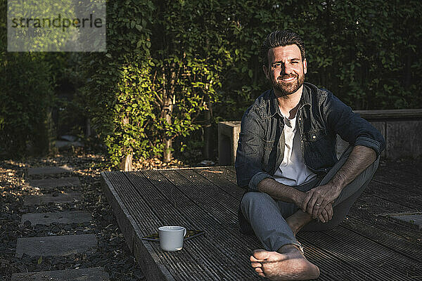 Glücklicher Mann mit Kaffeetasse sitzt auf der Veranda
