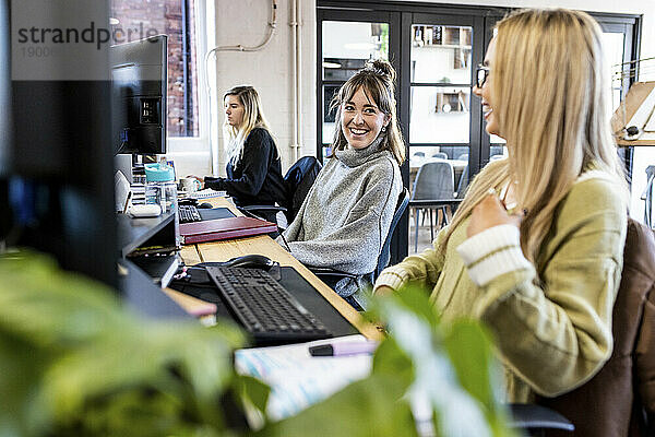 Glückliche Geschäftsfrauen sitzen zusammen am Schreibtisch im Büro