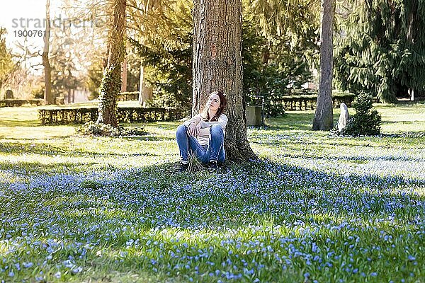 Junge lächelnde Frau auf einer Frühlingsblumenwiese sitzend