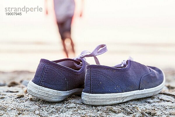 Zwei Turnschuhe am Strand mit laufenden Jungen im Hintergrund