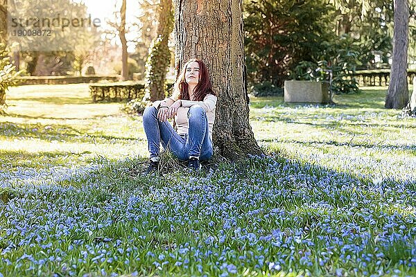 Junge lächelnde Frau auf einer Frühlingsblumenwiese sitzend