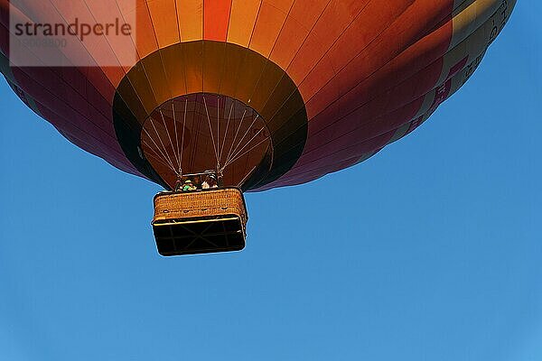 Heißluftballon im Flug mit unerkennbaren Menschen im Inneren an einem Tag mit blauem Himmel