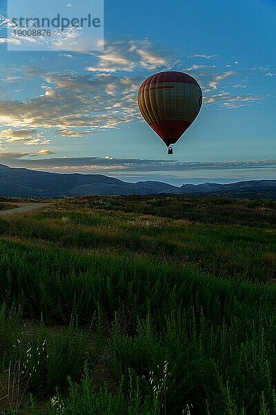 Heißluftballon  der in der Morgendämmerung an einem Tag mit blauem Himmel und bunten Wolken vom Boden abhebt