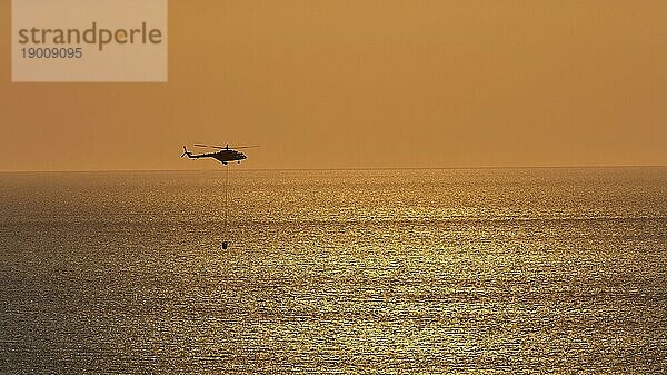 Hubschrauber  Helikopter  Lösch-Hubschrauber  dicht über dem Meer  Sonnenuntergang  Sonnenreflexionen auf dem Meer  Feuer  Falassarna  Westkreta  Kreta  Griechenland  Europa