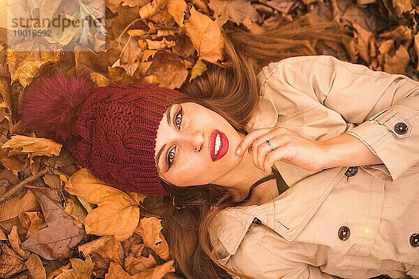Porträt einer Frau im Herbst  die auf braunen Blättern in einem Wald liegt und in die Kamera schaut