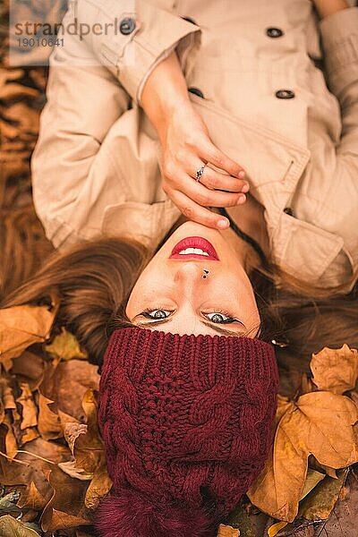 Porträt einer Frau im Herbst  die auf braunen Blättern in einem Wald liegt und in die Kamera schaut