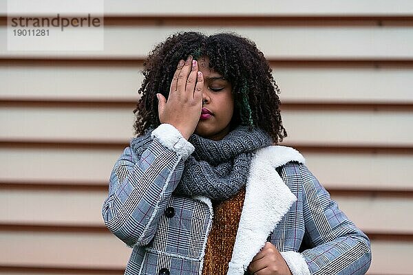 Schwarze ethnische Frau  die an einer grauen Wand eine Stop Rassismus Geste macht und dabei ihre Augen bedeckt