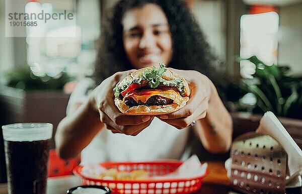 Lächelndes Mädchen zeigt einen Burger in einem Restaurant. Nahaufnahme einer Frau  die einen appetitlichen Hamburger in einem Restaurant zeigt