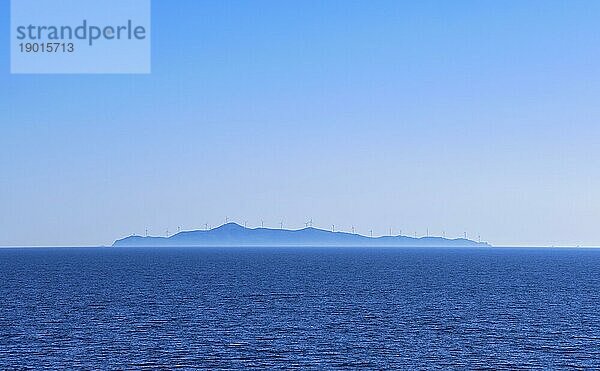 Meereslandschaft mit ruhigem azurblauem Meer und blauem Himmel ohne Wolken. Entfernte Insel in dunstigen Hintergrund mit Silhouetten von elektrischen Turbine Windmühlen punktiert. Mittelmeer  Griechenland  Europa