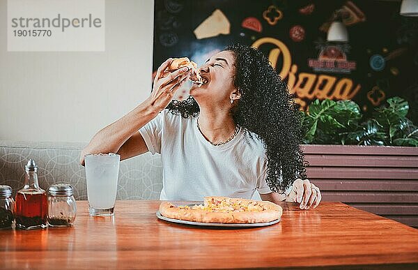 Lebensstil einer afro haarigen Frau  die eine Pizza in einem Restaurant genießt. Glückliche afrohaarige Frau isst Pizza in einem Restaurant