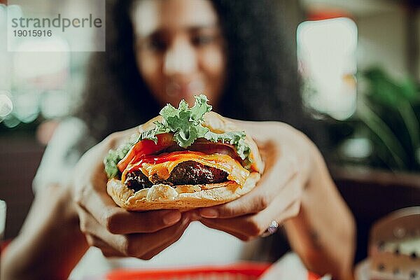 Nahaufnahme eines Mädchens  das einen appetitlichen Hamburger in einem Restaurant zeigt. Hände eines Mädchens zeigen Burger in einem Restaurant