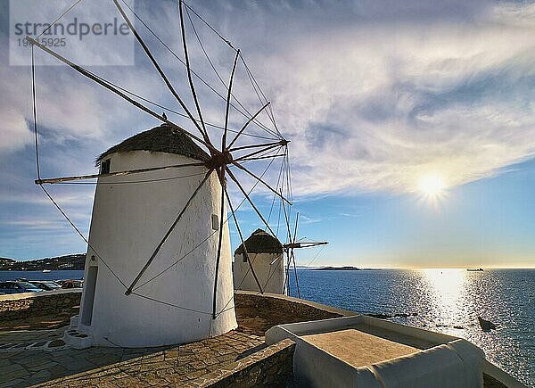 Berühmte Touristenattraktion von Mykonos  Kykladen  Griechenland. Zwei traditionelle weiß getünchte Windmühlen am Wasser und niedrige Sonne über dem Meer Horizont. Sommerabend  blauer Himmel  schöne Wolken. Reiseziel  ikonische Ansicht