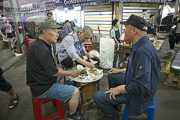 Alte Männer sitzen auf Plastikhockern und essen im Gwangjang Markt  traditioneller Straßenmarkt in Jongno-gu  Seoul  Südkorea  Asien