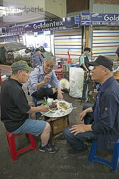 Koreanische Männer sitzen auf Plastikhockern und essen im Gwangjang Markt  traditioneller Straßenmarkt in Jongno-gu  Seoul  Südkorea  Asien
