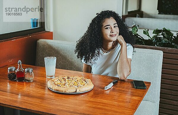 Schönes afro haariges Mädchen in einem Pizzeria Restaurant. Lebensstil eines afrohaarigen Mädchens  das in einer Pizzeria sitzt