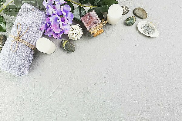Erhöhte Ansicht Handtuch Kerzen schrubben Flasche Blumen Spa Steine grau Hintergrund. Foto mit hoher Auflösung