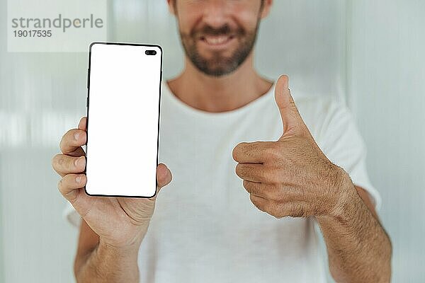 Bärtiger Mann zeigt Telefon mit Daumen nach oben. Foto mit hoher Auflösung