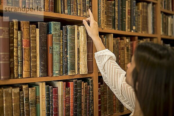 Frau wählt Buch aus Bücherregal Bibliothek. Schönes Foto