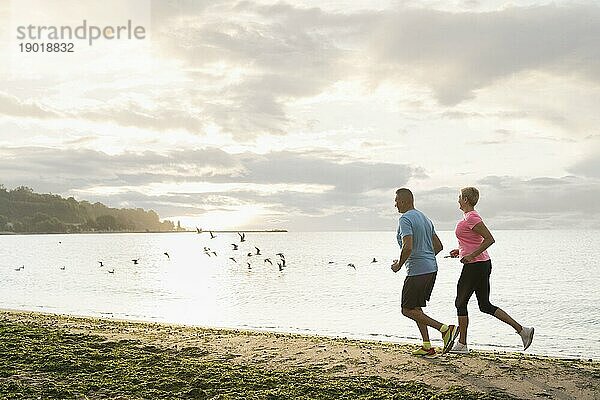 Seitenansicht älteres Paar joggt am Strand. Schönes Foto