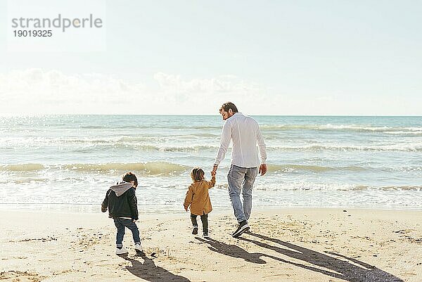 Mann mit Kleinkindern geht Richtung Meer