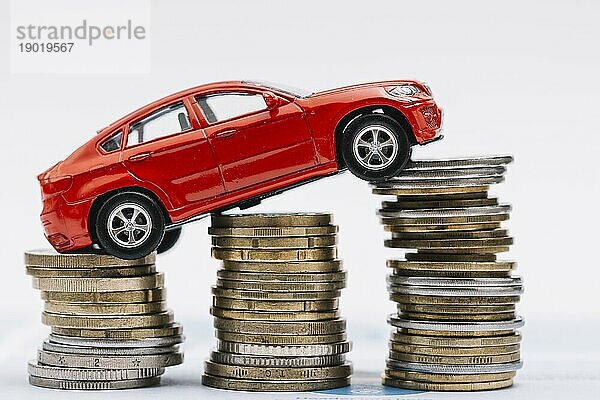 Rotes Spielzeugauto stapelt immer mehr Münzen vor weißem Hintergrund. Schönes Foto