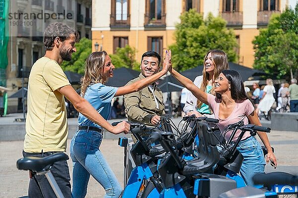 Eine Gruppe multiethnischer Freunde in der Stadt neben Leihfahrrädern  die sich amüsieren und sich zuprosten